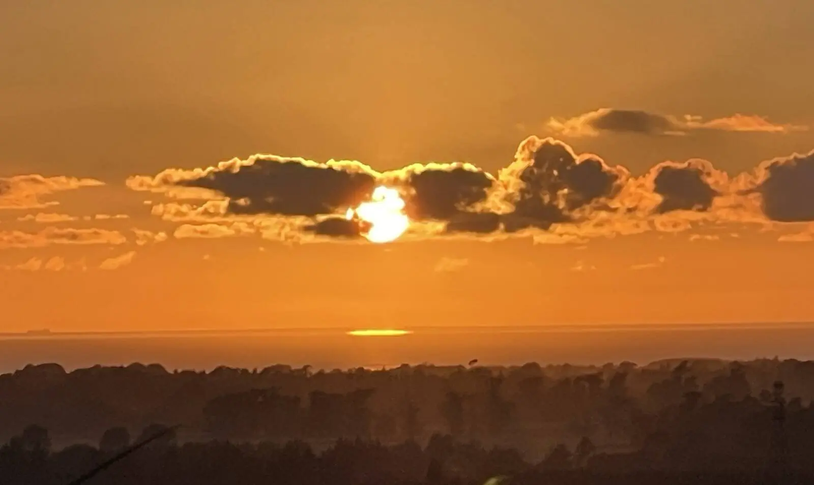 A golden sunset with the sun low between banks of cloud over darkening plains